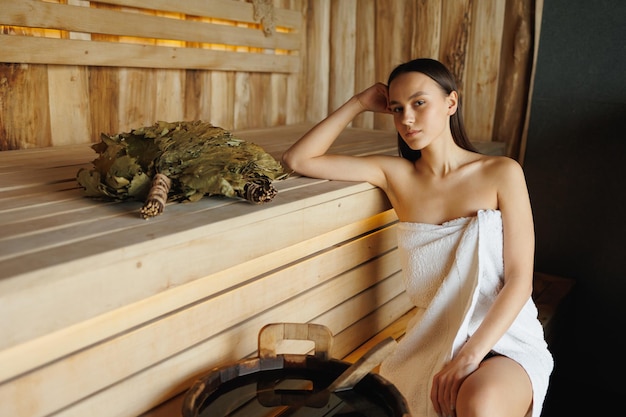 Young woman sitting on a wooden bench in a traditional sauna