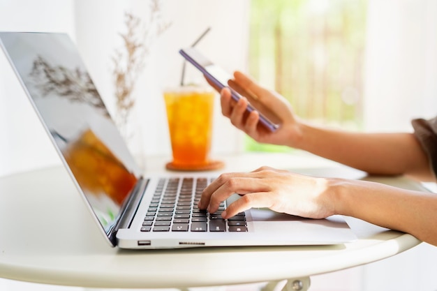 Young woman sitting and working on laptop and smart phone at coffee shop