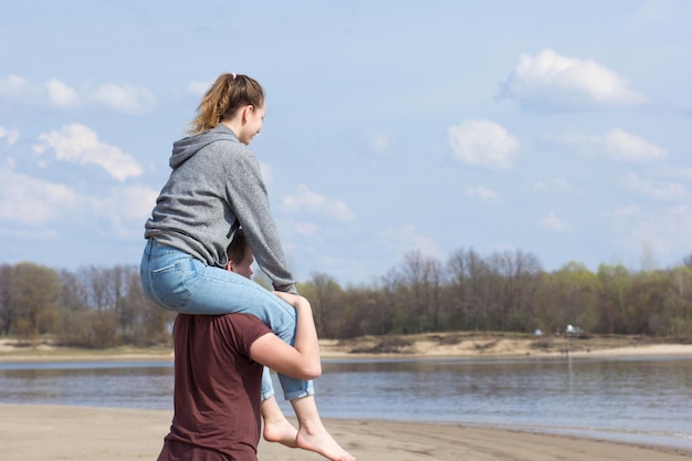 Young woman sitting on young man shoulders in the springtime near river