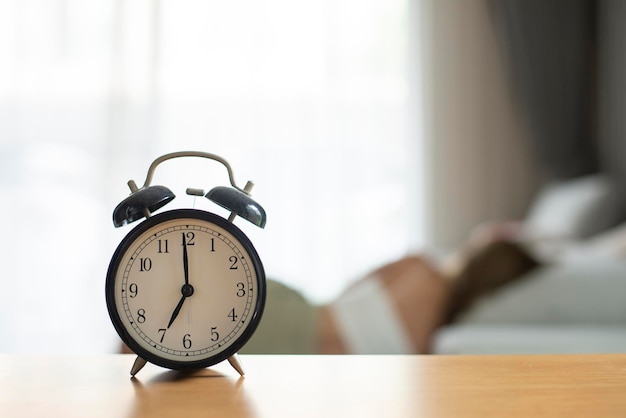 Young woman sleeping on sofa bed in living room with alarm clock in morning