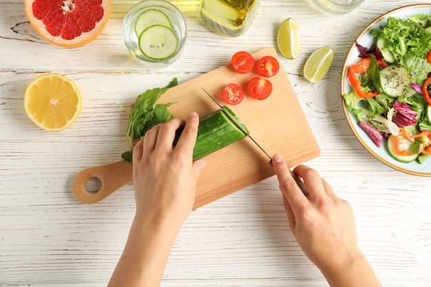 Young woman slices cucumber for salad on wooden