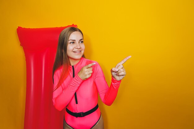 Young woman slim body pink one piece swimsuit on pink air mattress isolated on bright yellow color studio background summer hotel swimming pool sea vacation sun tanning concept Place for text