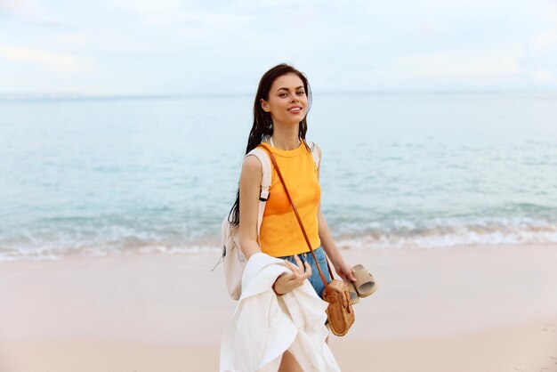 Young woman smile with teeth after swimming in the ocean with a backpack in wet clothes walking along the beach summer vacation on the island by the ocean in Bali sunset