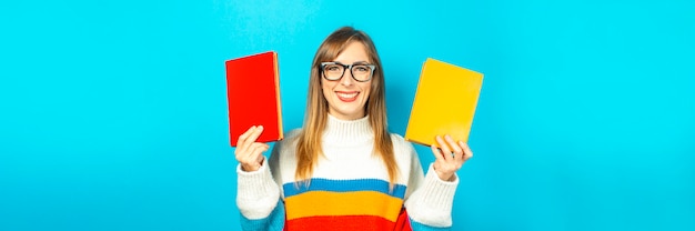 Young woman smiles and holds books in her hands on a blue background. Concept of education, college, session, exam, career choice. Banner