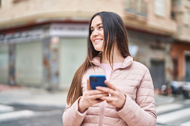 Young woman smiling confident using smartphone at street