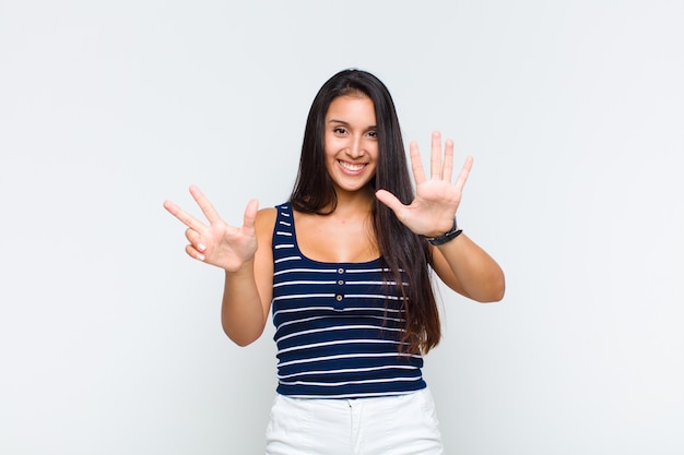 Young woman smiling and looking friendly, showing number eight or eighth with hand forward, counting down