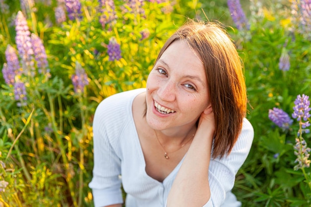 Young woman smiling outdoor beautiful brunete girl resting on summer field with blooming wild flower