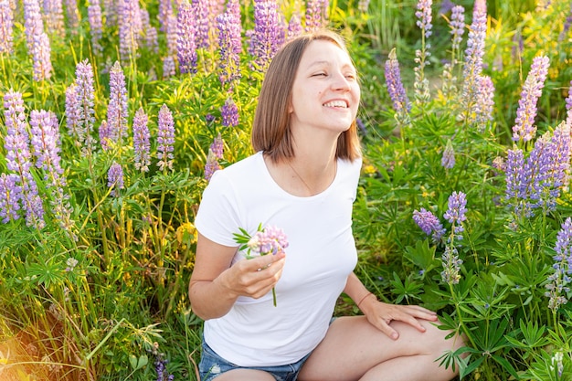 Young woman smiling outdoor beautiful brunete girl resting on summer field with blooming wild flower...