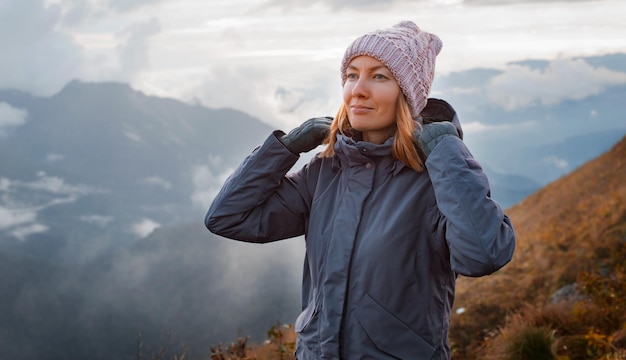 Young woman smiling with a backpack in a hat admiring looks at the mountains