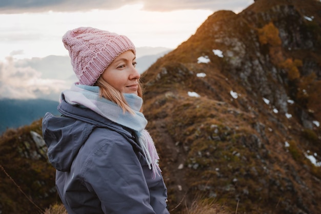 Young woman smiling with a backpack in a hat admiring looks at the mountains