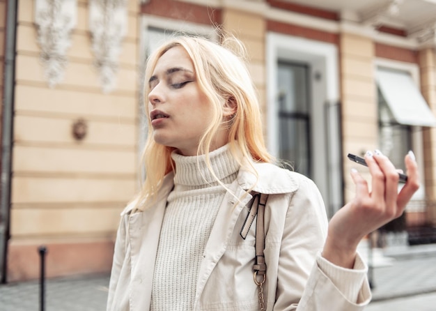 Young woman smokes smoke an electronic cigarette in the city