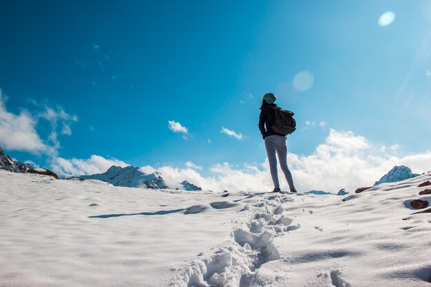 A young woman on a snow top amid a blue sky. White clouds.