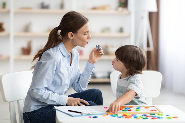 Young woman speech therapist teaching little boy with pronounciation deffects to say sound u during