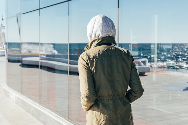 Young woman in sports clothes and a hood walking on the beach on a sunny morning