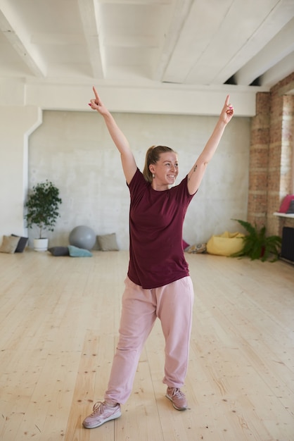 Young woman in sports clothing raising her hands and smiling she exercising in dance studio