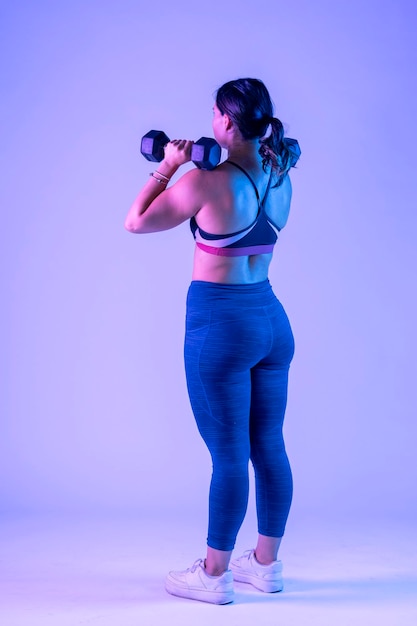 Young woman in sportswear from behind doing shoulder press with two dumbbells