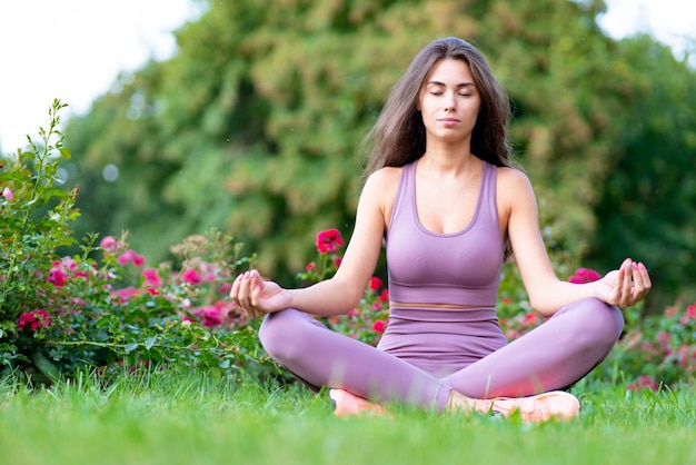 Young woman in sportswear meditating in yoga lotus position sitting outdoors in the garden beautiful...