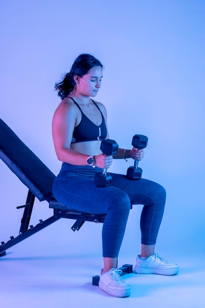 Young woman in sportswear sitting on a bench with two dumbbells in her hands