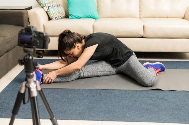 Young woman in sporty outfit doing some stretching exercises and recording it on camera