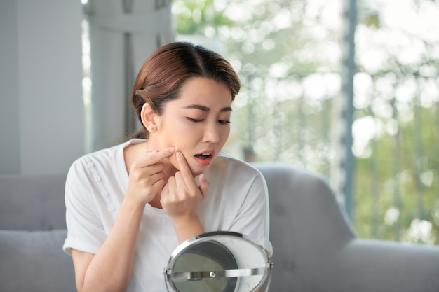 Young woman squeeze her acne in front of the mirror