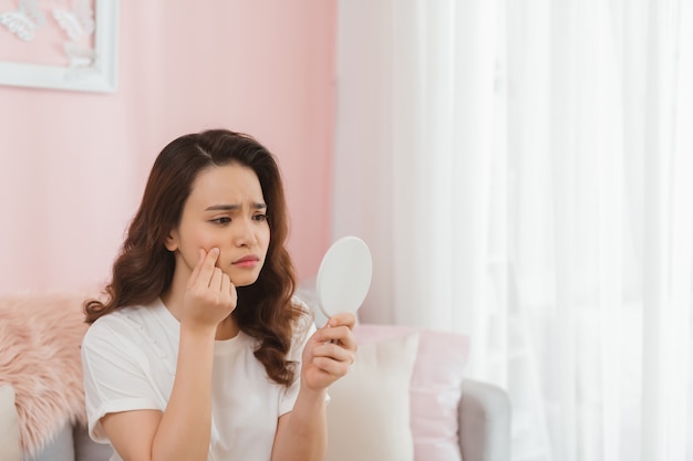 Young woman squeezing pimples in front of mirror