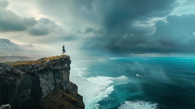 Young woman standing on a cliff with arms raised in the air looking out at the vast ocean She is wearing a blue tank top and black leggings