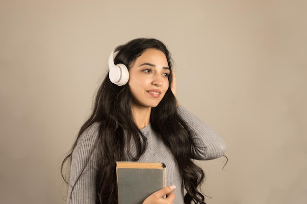 Young woman standing in headphones holding a book