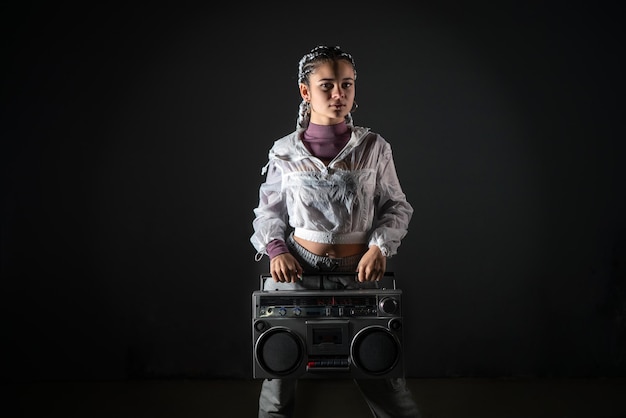 Young woman standing and holding retro tape recorder while looking at camera in studio shot