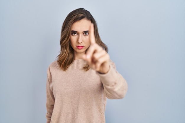 Young woman standing over isolated background pointing with finger up and angry expression showing no gesture