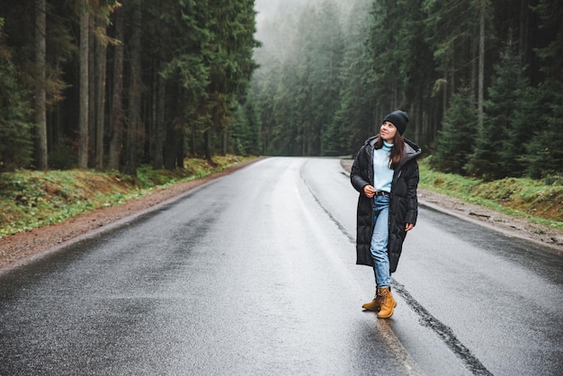 Young woman standing at the middle of the road in winter mountains forest