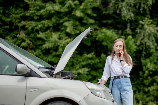 Young woman standing near broken down car with popped up