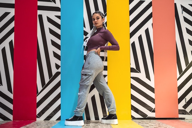 Young woman standing and posing sideways while looking at camera against an abstract wall