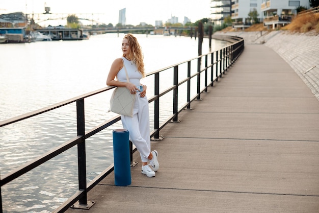 Photo young woman standing at the river embankment and looking away after yoga training