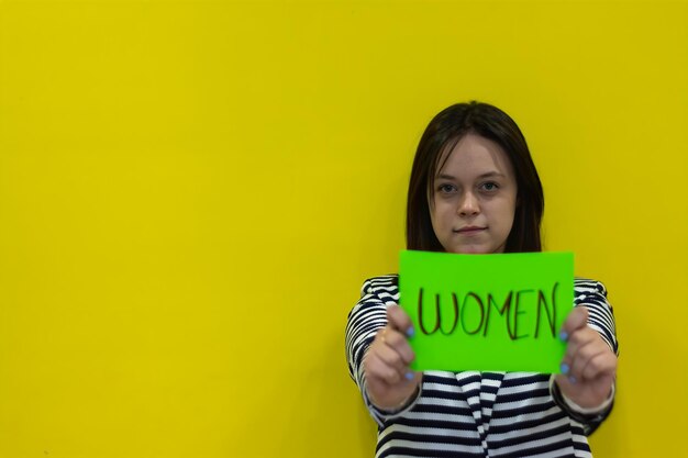 A young woman standing showing a sign with the word quotwomenquot on a yellow background