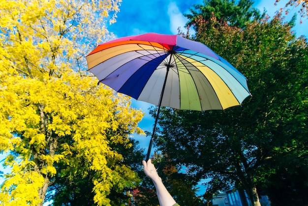 Young woman standing with a multicolored umbrella and rotates it against with a blue sky