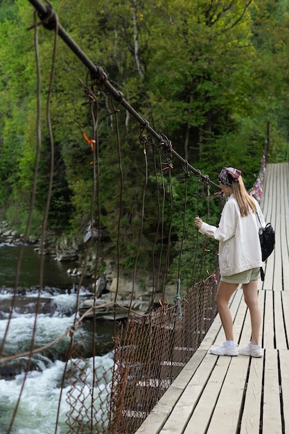 A young woman stands on a bridge looking down at a flowing river Girl tourist enjoys nature vertical image