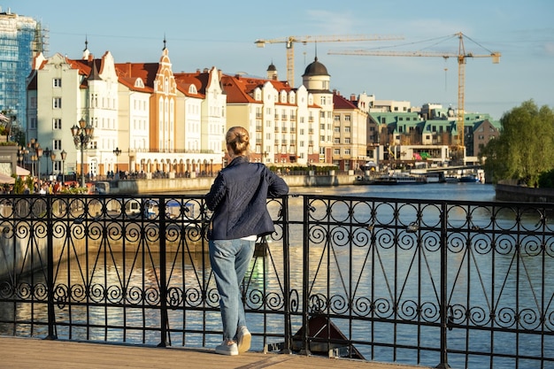 Young woman stands on bridge and looks at city embankment