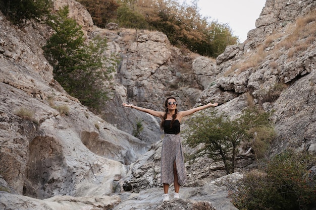 A young woman stands with her hands up in the fresh air in a mountainous area A smiling woman greets the sun