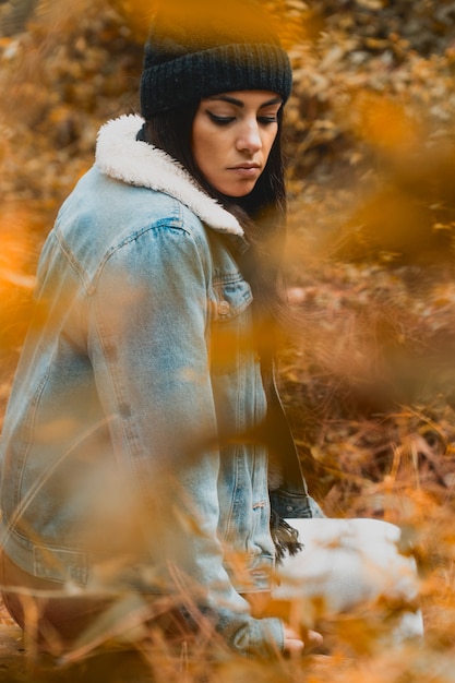 Young woman staring through a fall colors forest with season clothes