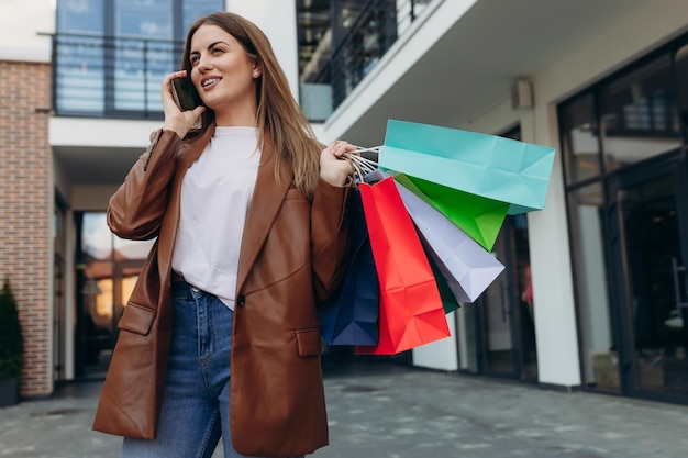 Young woman on the street with colored bags talking on a cell phone