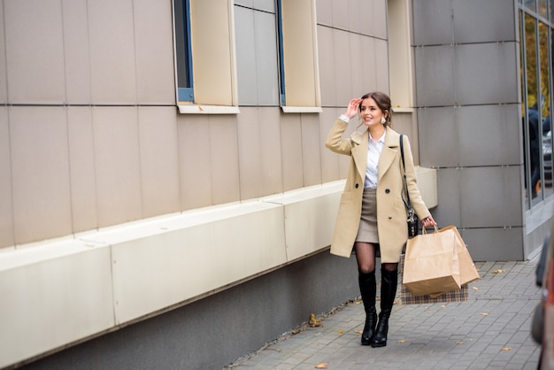 Young woman at the street with shopping bags. Beautiful emotional girl in a coat. Black friday sale concept. Street photo in the metropolis.