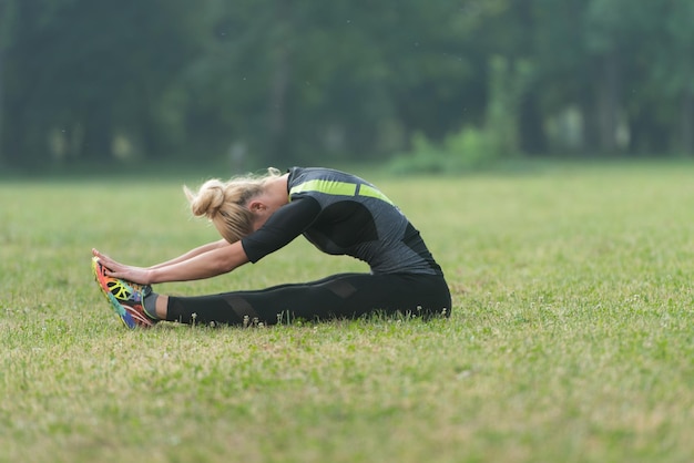 Young Woman Stretching Before Running In Wooded Forest Area - Training And Exercising For Trail Run Marathon Endurance - Fitness Healthy Lifestyle Concept