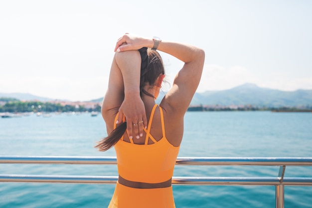 Young woman stretching with an orange sport set at the port