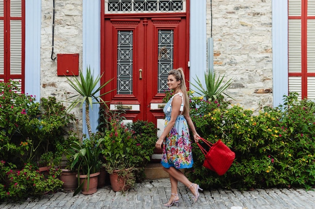 Young Woman Strolling Past Historic House with Red Doors and Bunch of Different Plants and Flowers in Mediterranean Village