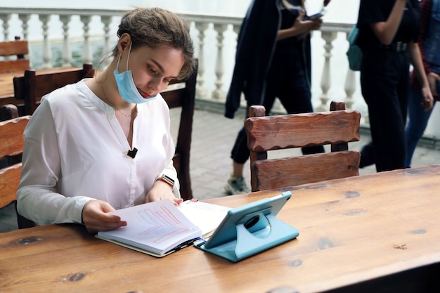 Young woman student sits outdoors at the table and works with notes in notebook