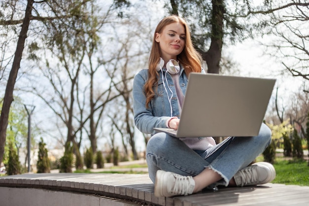 Young woman student sits in the park on a bench with a laptop