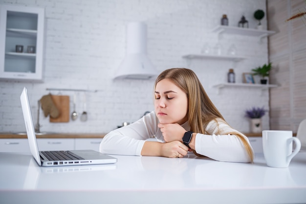 Young woman studies at home in the kitchen on a laptop. Work remotely from home