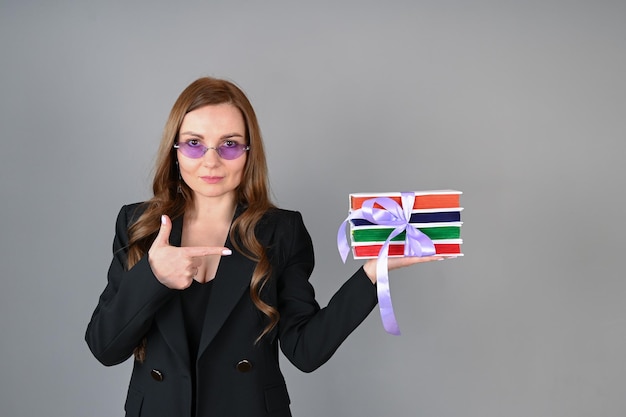 A young woman in stylish glasses points to a stack of books The concept of online learning distance learning bookstore advertising