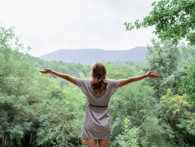 Young woman in summer dress standing on a big rock in the forest