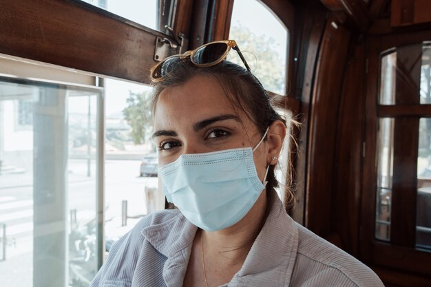 Young woman on sunglasses and a face mask inside an old train in porto smiling to camera on indie clothes, travel and new experiences concept